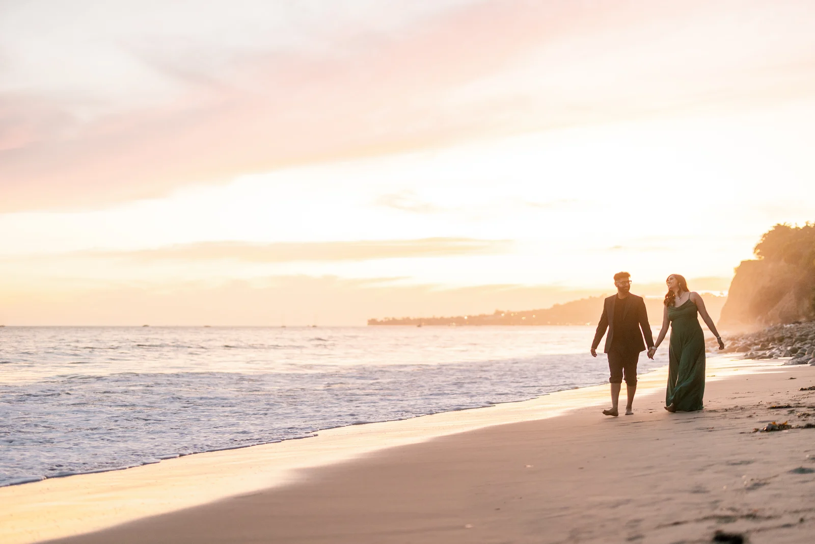 Arpita and Varad sharing a smile as they walk hand in hand along the shoreline at sunset