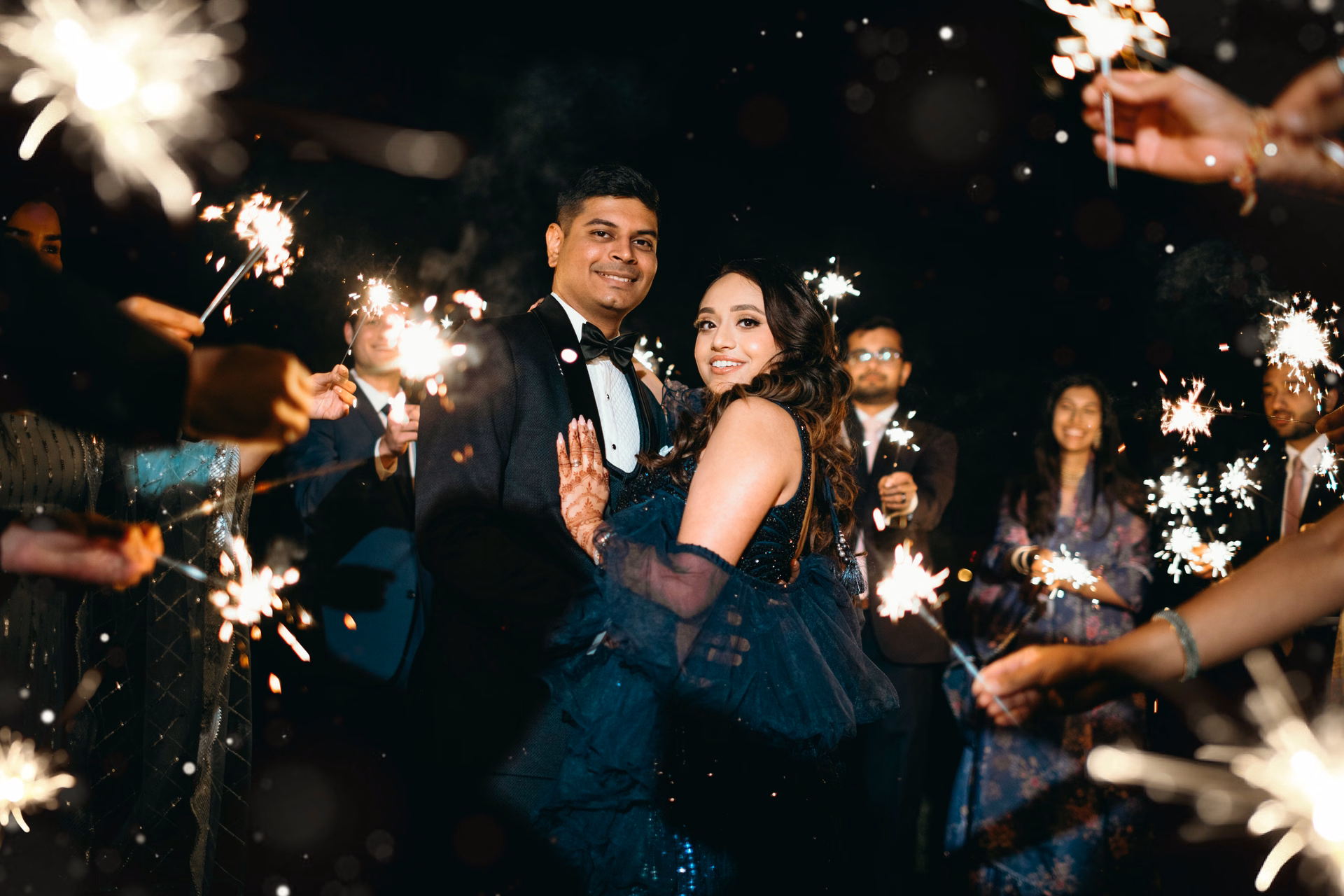Purna & Mayur celebrating together, surrounded by their guests holding sparklers