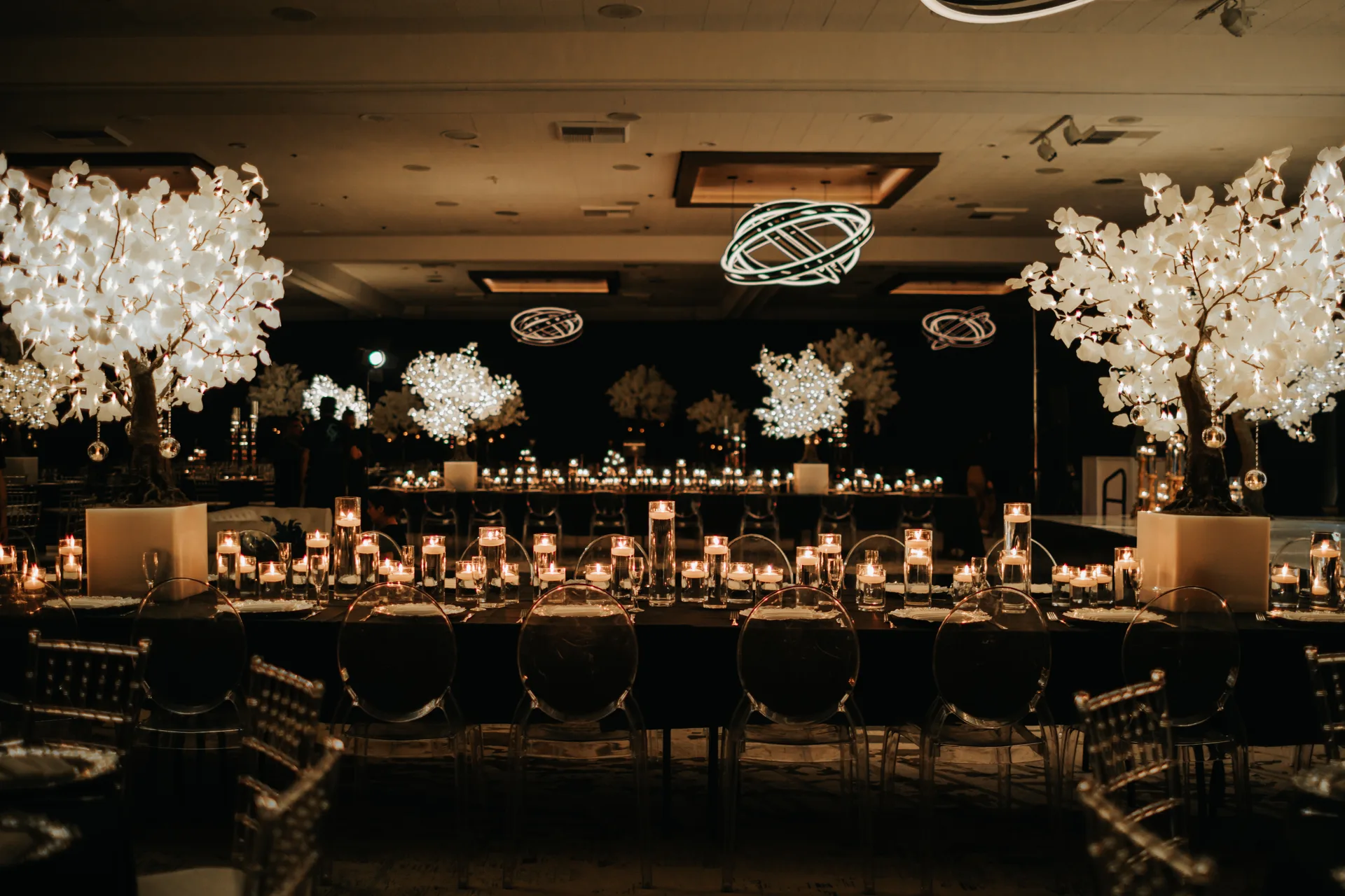 A candlelit reception with luminous floral trees, layered table settings and an expansive dining environment