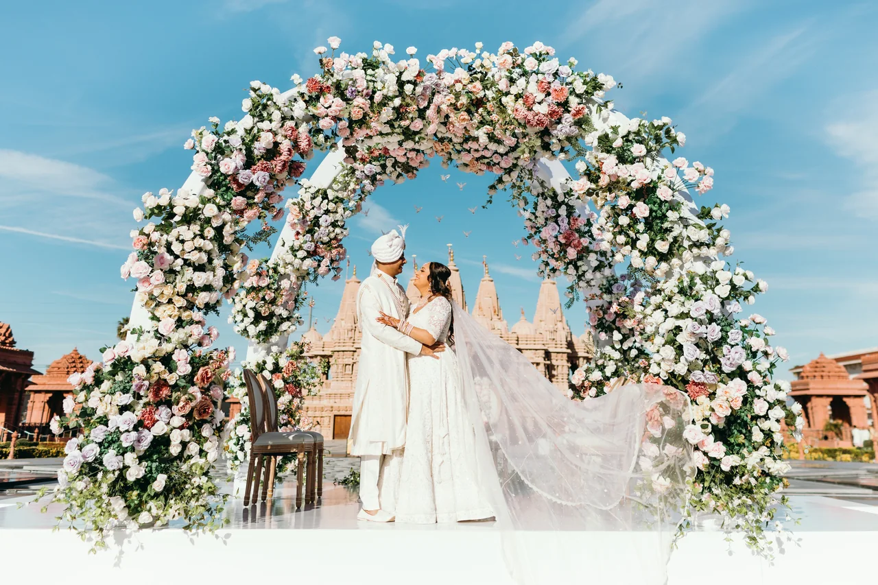 Purna and Mayur beneath the floral ceremony arch, her veil lifted in the breeze